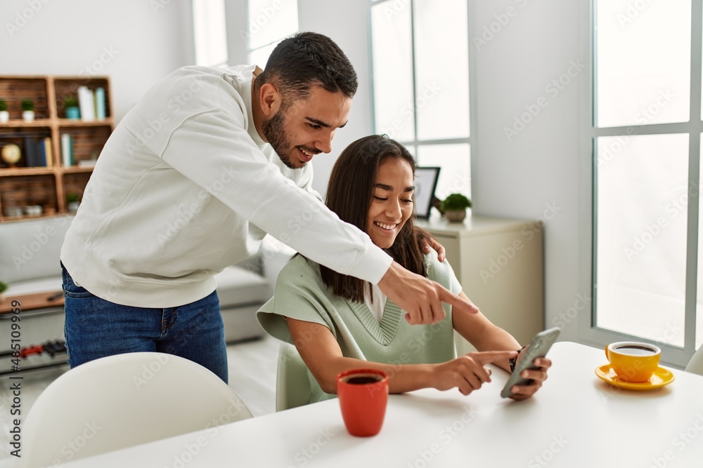 Young latin couple smiling happy using smartphone at home.