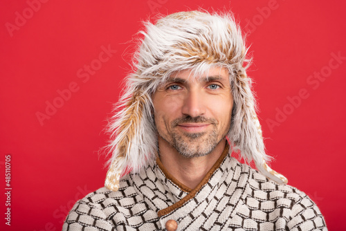 smiling man in sweater and earflap on red background, winter