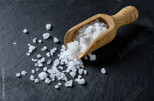 Sea salt in a wooden scoop on a black background. Coarse salt.