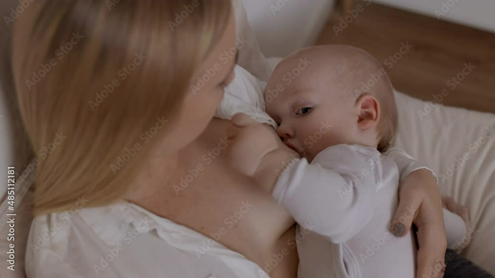 Young blonde woman feeding with breast and kissing her baby boy. Concept of breastfeeding, maternity and happy parenting. Time for togetherness, love and rest for mother and little son Young blonde woman feeding with breast and kissing her baby boy. Concept of breastfeeding, maternity and happy parenting. Time for togetherness, love and rest for mother and little son