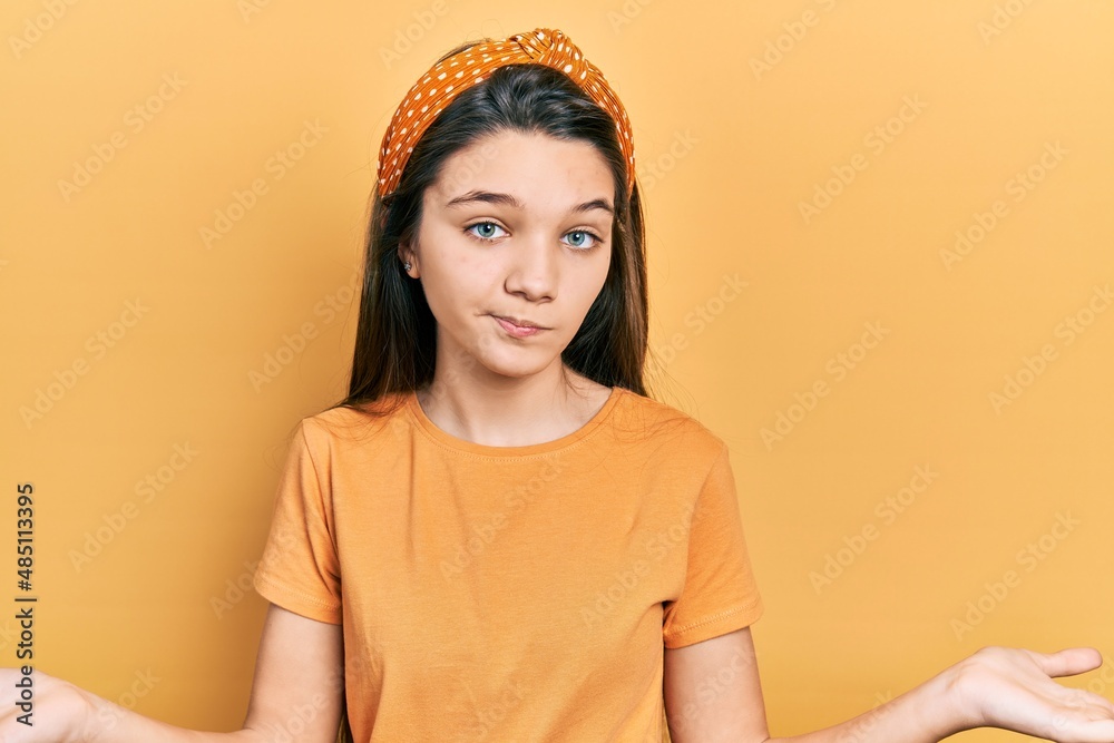 Young brunette girl wearing casual orange t shirt clueless and confused expression with arms and hands raised. doubt concept. Young brunette girl wearing casual orange t shirt clueless and confused expression with arms and hands raised. doubt concept.