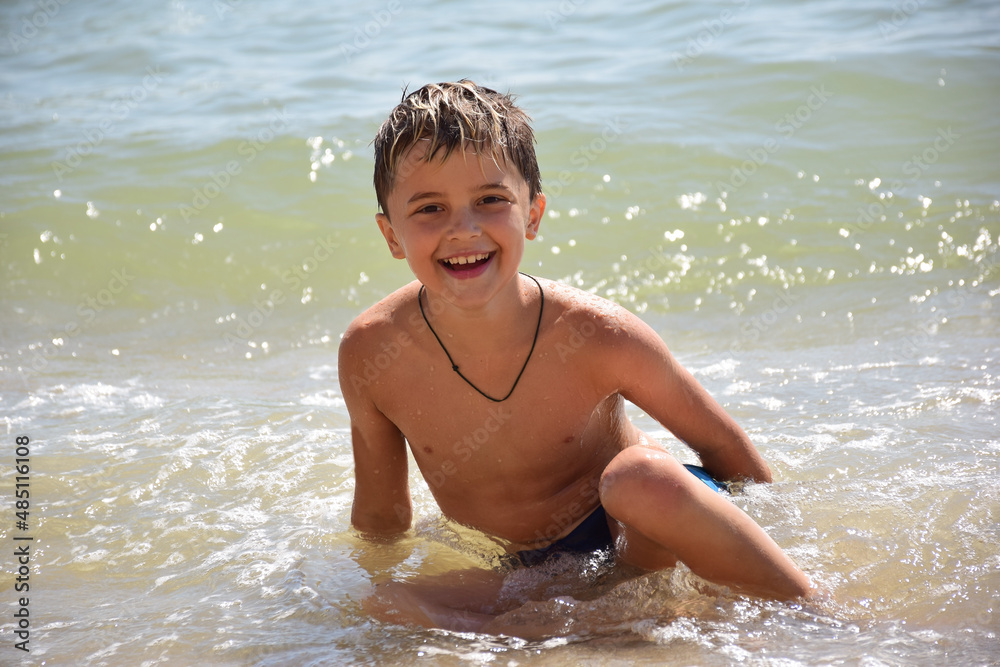 A white race child splashes near the shore on the sea beach and smiles A white race child splashes near the shore on the sea beach and smiles