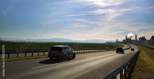 Samochody na drodze szybkiego ruchu, krajobraz wiejski przed zachodem słońca, fabryka, zakład.
