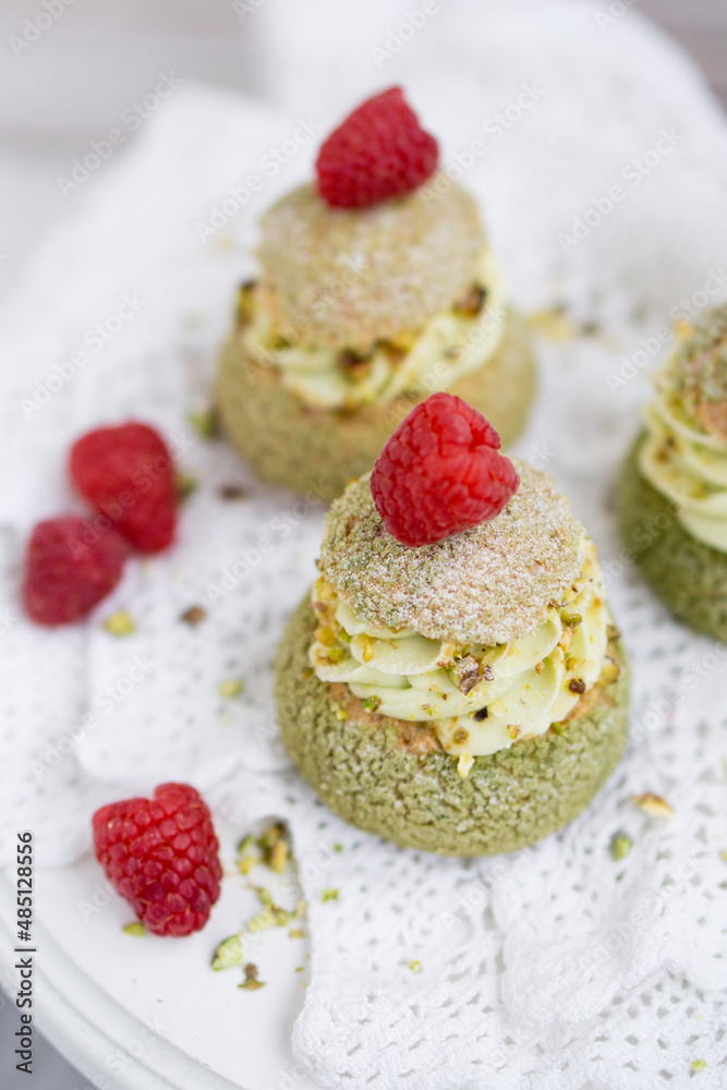 Choux with pistachio cream and raspberry french dessert on white background close up selective focus Choux with pistachio cream and raspberry french dessert on white background close up selective focus