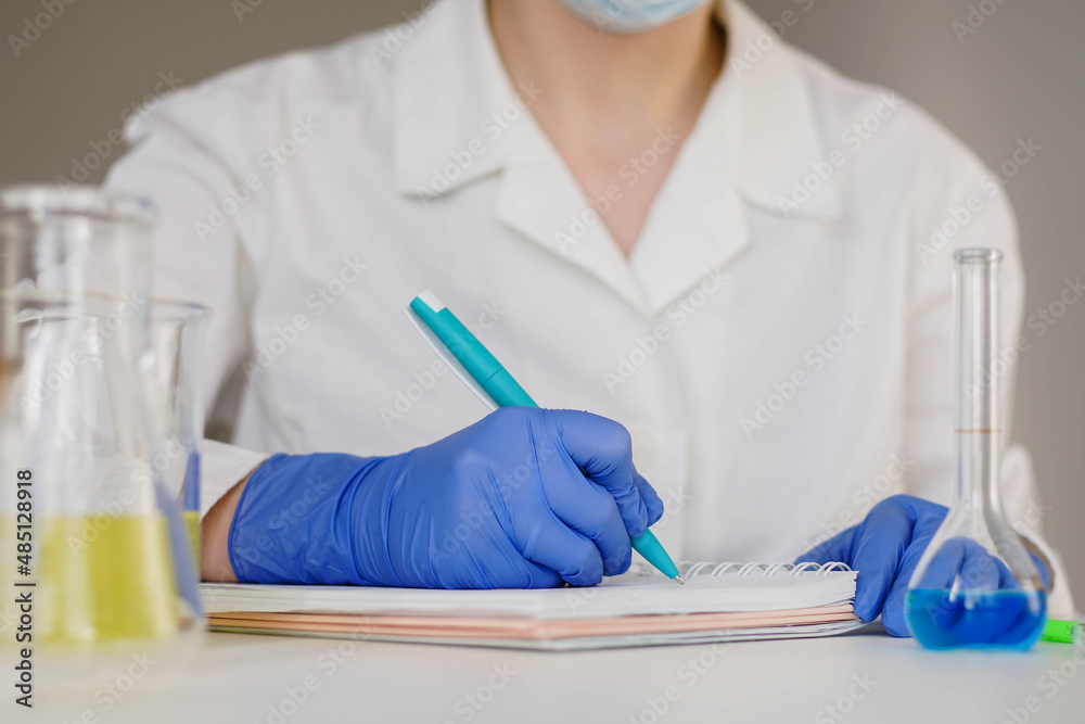 Woman pharmacist in blue gloves writes down the results of research in a notebook. Woman pharmacist in blue gloves writes down the results of research in a notebook.