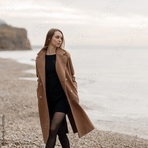 portrait of a young happy woman in coat and glasses outdoor on the beach autumn spring