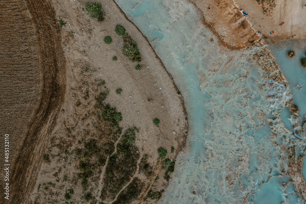 Obraz premium The aerial drone view of people swimming and relaxing in Saturnia hot springs in Tuscany, Italy. Nature, hot spring lagoons, lush forests and fields on a hot summer day