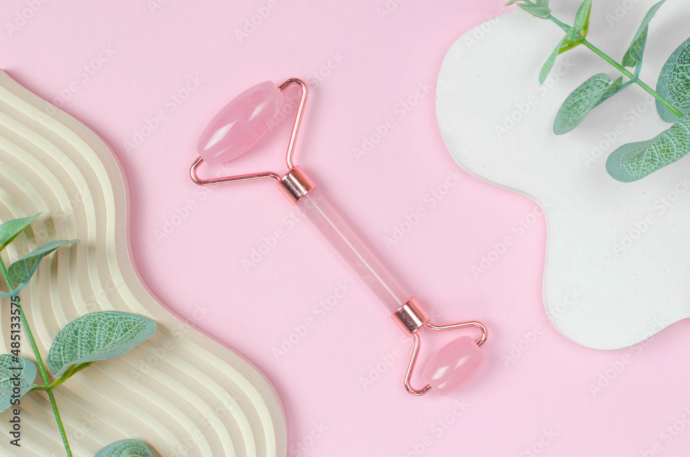 Roller jade facial massager on pink background with geometric shapes. Gua Sha face massage tools on pink background with green leaves Roller jade facial massager on pink background with geometric shapes. Gua Sha face massage tools on pink background with green leaves