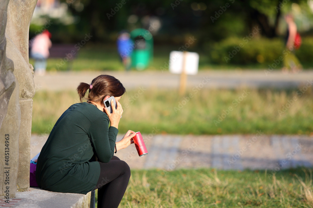 Kobieta z czerwoną puszką napoju rozmawia przez telefon.
 - obrazy, fototapety, plakaty 