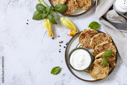 Zucchini fritters. Vegetarian zucchini pancakes with cheese, served with sour cream on a rustic wooden table. Healthy food, low calories keto dieting meal. Top view flat lay background. Copy space.