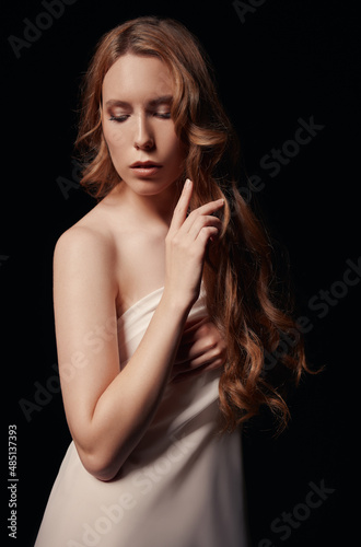 Dramatic portrait of lovely young sad girl against black background. Sorrowful woman among the dark