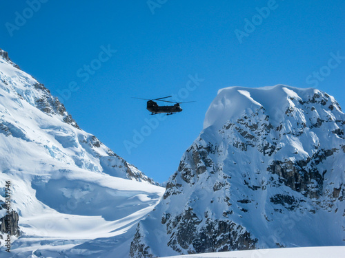 Military Chinook Helicopter contrasted against blue sky and snowcapped mountains in the Alaska Range