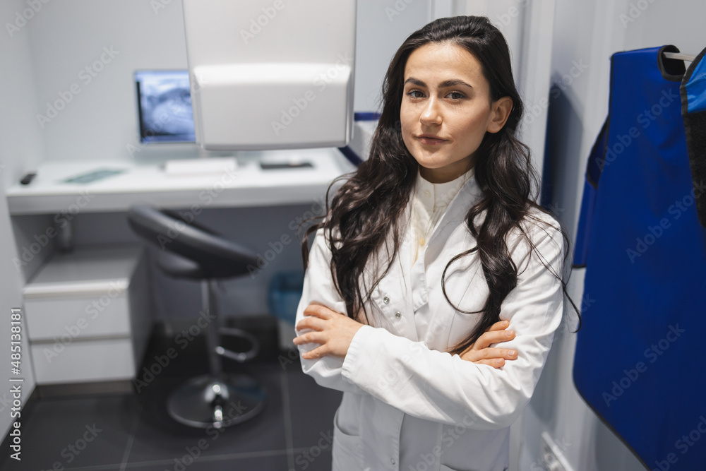 Portrait of serious female medic with arm crossed in CT scan room. Woman near the tomograph Portrait of serious female medic with arm crossed in CT scan room. Woman near the tomograph