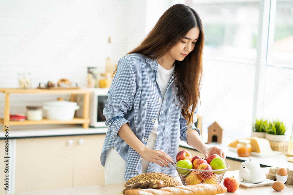 Young pretty Asian women choose fruit and apple for her breakfast inside of the kitchen. Good food with nutrition for healthy eating or diet for weight control.