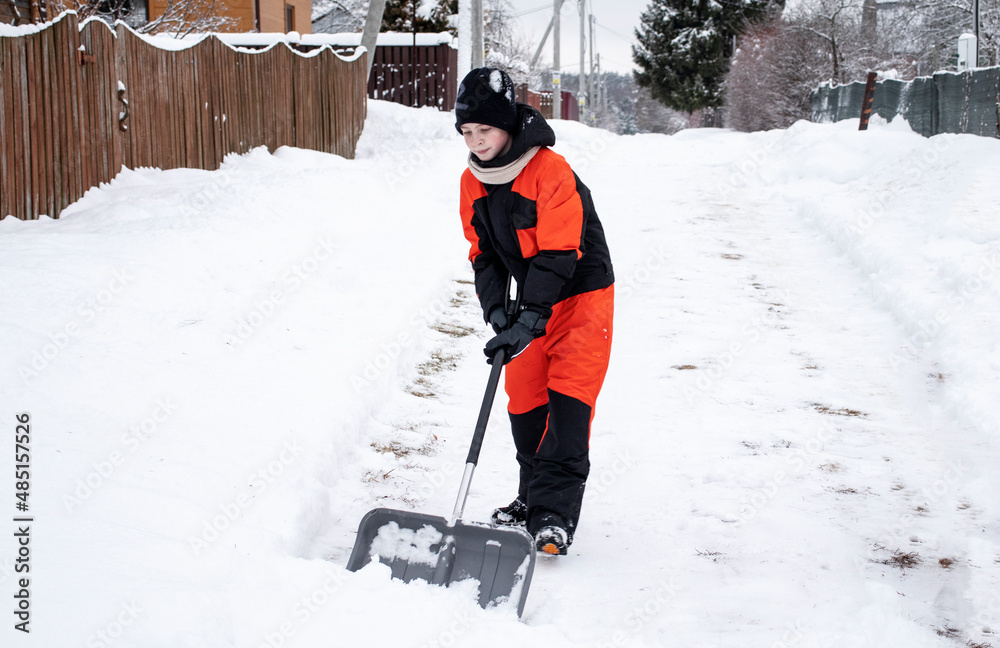 teen boy clearing snow with a shovel on the road in the village