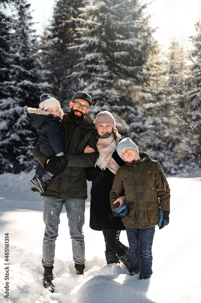 young family on a walk in the winter park. father with his wife and small children stand in bliss against the backdrop of the forest