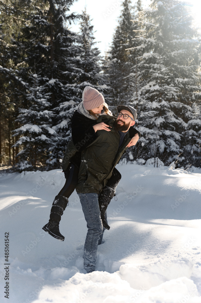 Young couple on the snow in winter in the park. love and vacation concept - happy couple hugging and laughing outdoors in winter