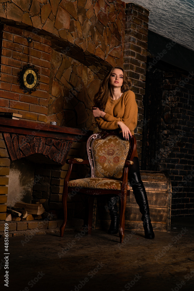 A young girl sitting in a chair near a fireplace looking determined