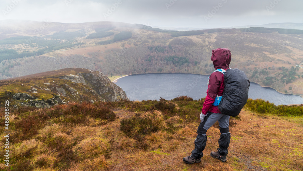 Woman from behind looking towards Lough Tay (Guinness Lake) from Luggala peak in the Wicklow mountains Ireland. Cloudy and wet day