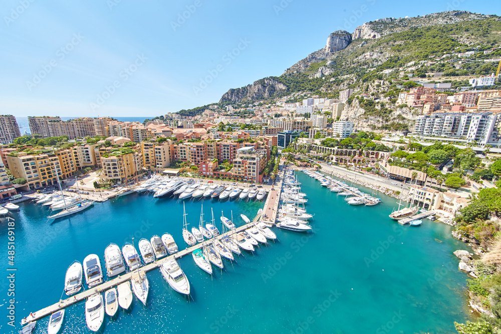 Panoramic image of Port Fontvieille - Monaco, top view from Monaco Ville, azur water, sun reflections on the water, harbour at sunny day, luxury apartments, a lot of yachts and boats, mountain
