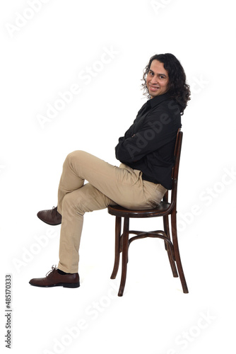 side view of a man with shirt, shoes and pants sitting on chair arms and legs crossed and looking at camera on white background