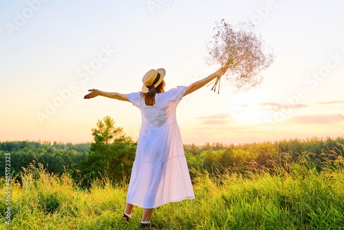 Back view of romantic woman in a white dress with a straw hat enjoying sunset