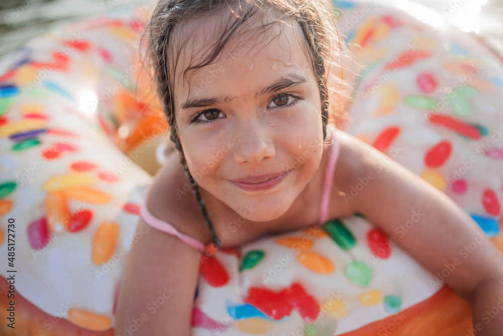 A close up portrait of smiling tween girl swims with a big donut shaped inflatable ring on a lake on a hot summer day, happy summertime, local vacation, cottagecore, countryside A close up portrait of smiling tween girl swims with a big donut shaped inflatable ring on a lake on a hot summer day, happy summertime, local vacation, cottagecore, countryside