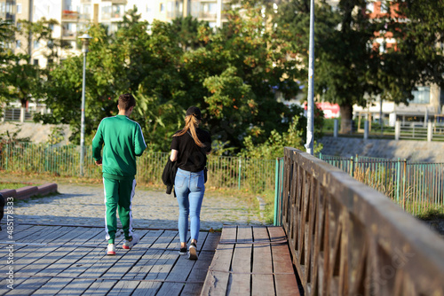 Para młodych ludzie spaceruje deptakiem, chodnikiem w parku, drewniany most, Wrocław. 