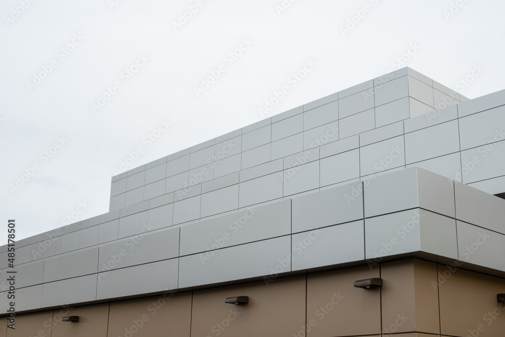 The exterior wall of a contemporary commercial style building with aluminum metal composite panels and glass windows. The futuristic building has engineered diagonal cladding steel frame panels.