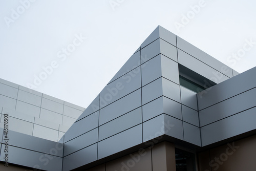 The exterior wall of a contemporary commercial style building with aluminum metal composite panels and glass windows. The futuristic building has engineered diagonal cladding steel frame panels. photo