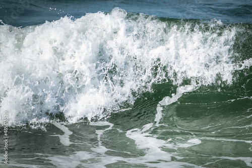 A large green colored rip wave rolling along the beach in the cold North Atlantic Ocean. There's spray coming off the foam along the rip of the wave. The background is a dark majestic blue sea.