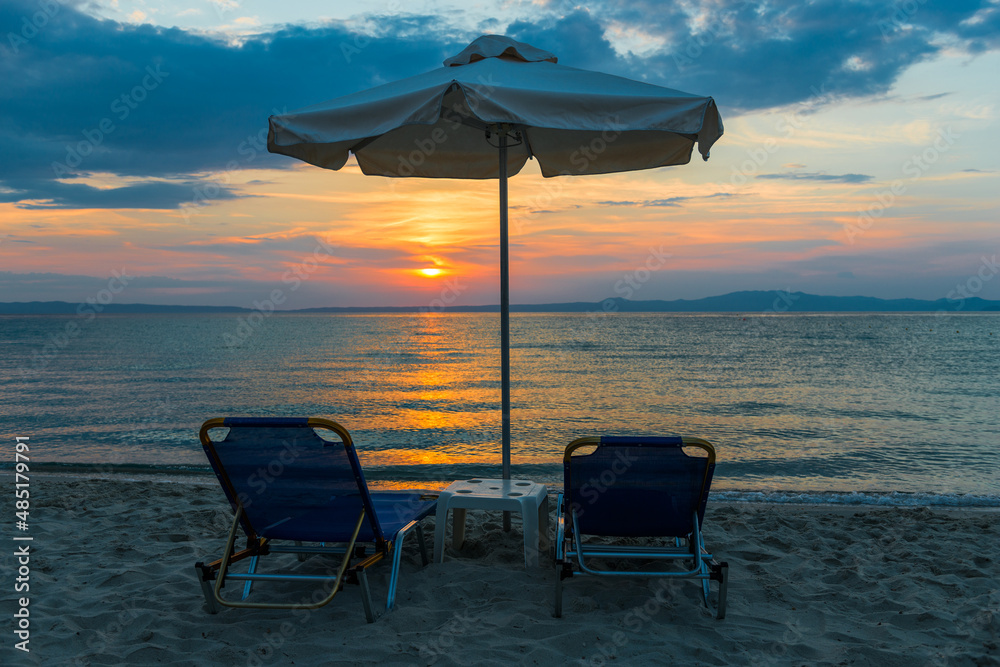 Beautiful sunset seascape with beach chairs and umbrella on the coast, Greece
