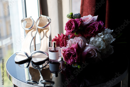 Beautiful wedding bouquet of roses and greenery, huge shoes and perfume on the table photo