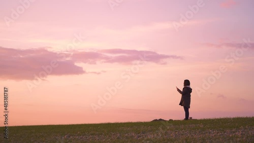 Woman take a photo by smartphone on a hill in the sunset, low angle shot