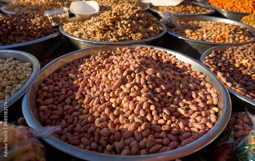 Close up of stainless steel scoop with roasted piled peanuts on display at street market. Peanuts in plastic bag ready for sale. High quality photo