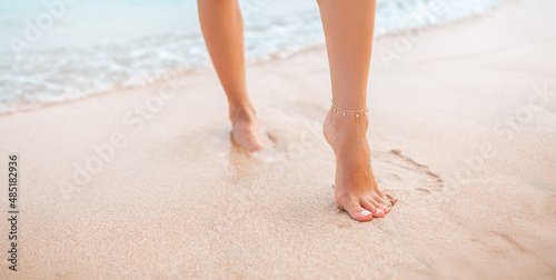 Female legs walking along the seaside barefoot, close-up of the perfect tanned legs of a girl coming of the water after swimming. Woman relaxing on vacation, enjoying time at the beach, summer concept