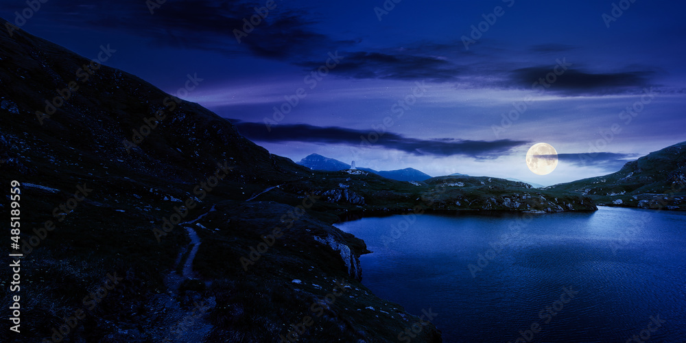 mountain landscape with lake in summer at night. beautiful travel destination of fagaras ridge, romania. scenic nature scene in full moon light. outdoor adventure in green environment