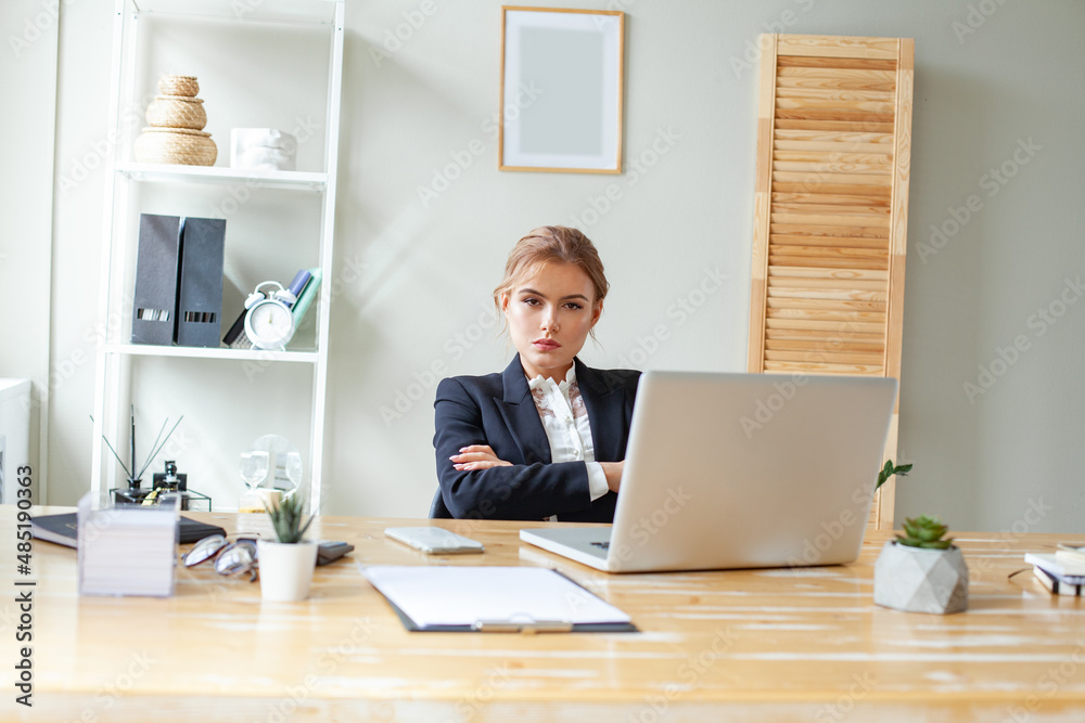 Serious smart business woman in black suit sitting with arm crossed in her office Serious smart business woman in black suit sitting with arm crossed in her office