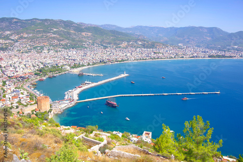 Turkey. Alanya 09.14.21. View from a height of a city among the mountains to the port and ships on the pier, as well as a lighthouse.