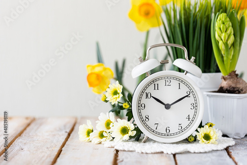 Spring change, Daylight Saving Time concept. White alarm clock and flowers on the wooden table. Copy space