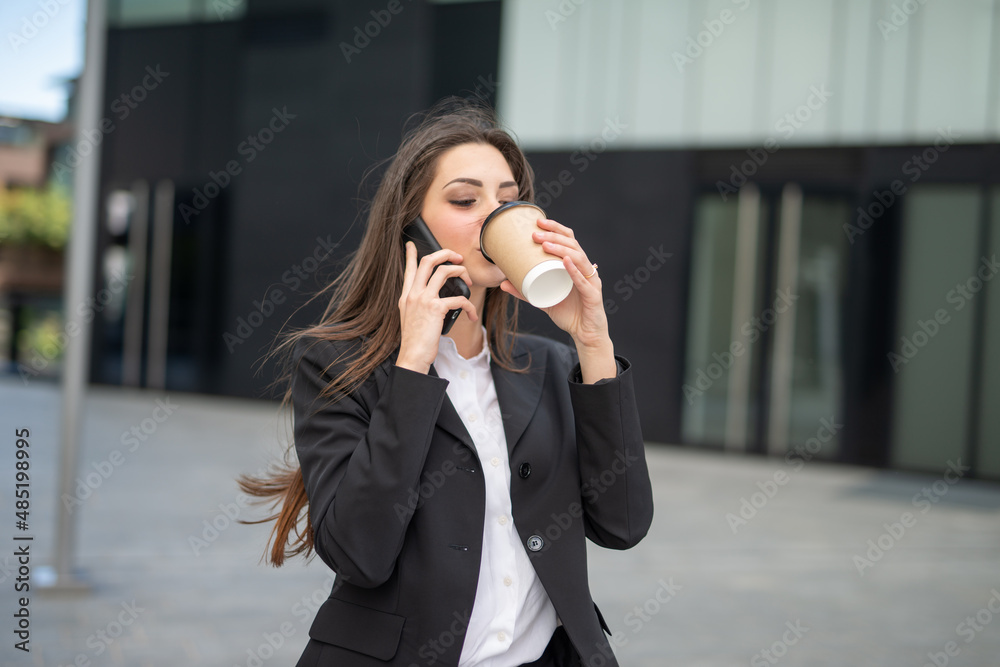 Businesswoman talking on the phone in a city street while drinking coffee