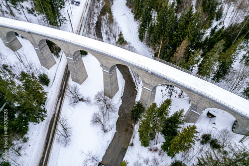 Wiadukt kolejowy w górach zimą nad rzeką i drogą. Wisła, Beskid Śląski w Polsce
