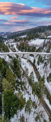 Wiadukt kolejowy w górach zimą nad rzeką i drogą. Wisła, Beskid Śląski w Polsce