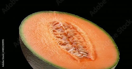 One half of a cantaloupe melon is rotating. Isolated on black background.