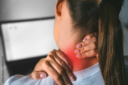 Neck pain after working on computer. Young woman massaging neck to relieve pain after working on pc photo