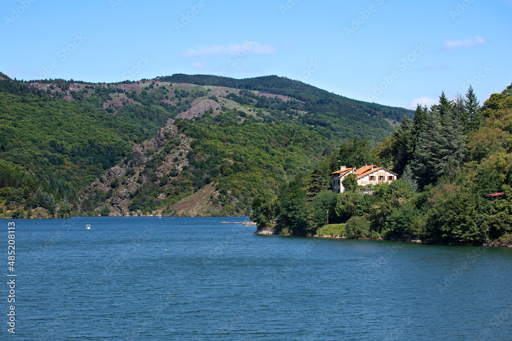 Lac d'altitude au-dessus d'un barrage avec hôtel restaurant de tourisme pour des vacances en été en montagne dans les Cévennes en France.