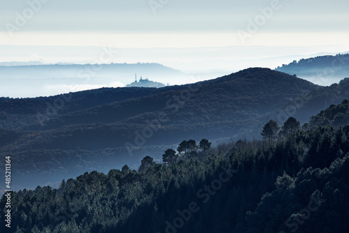 Vallée sauvage et boisée dans la brume matinale de l'automne avec relai télécom au sommet d'une montagne.