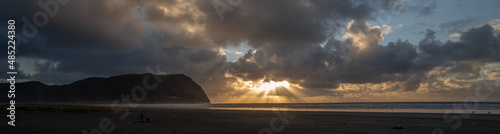 A panorama image of a sun burst at sunset and Tillamook Head headland and the beach at Seaside Oregon.
