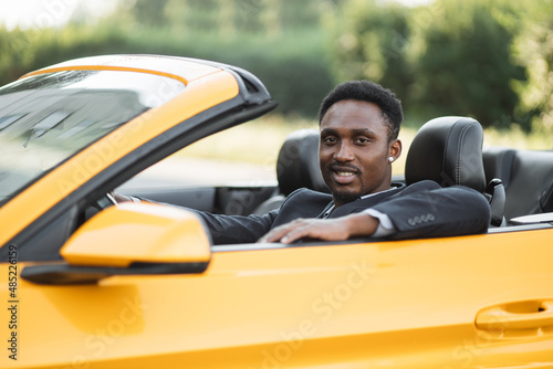 Car side window. Young handsome bearded African businessman driver happy smiling driving sport yellow car. Handsome young man excited about his new vehicle. Positive face expression