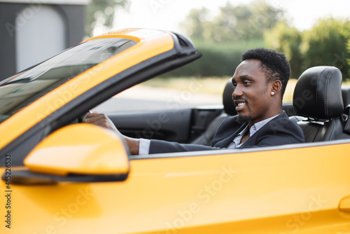 Mature African American business man sitting in the luxury sport vehicle and smiling looking aside. Portrait of an handsome smiling African man driving his car with formal suit